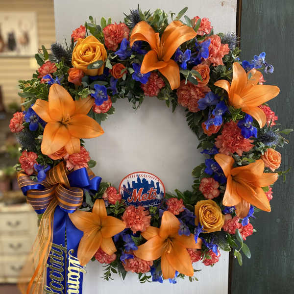 Circular floral wreath with orange lilies, roses, and blue flowers