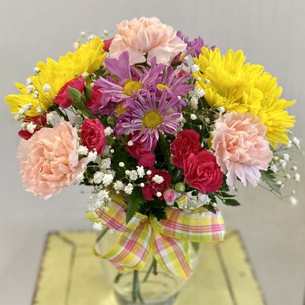 Colorful bouquet of carnations and daisies in a glass vase with a plaid ribbon