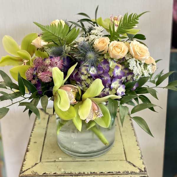 Mixed bouquet in a glass vase with orchids, roses, and purple blooms