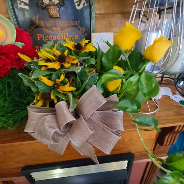 Yellow roses and black-eyed Susans in a burlap-wrapped container with a bow