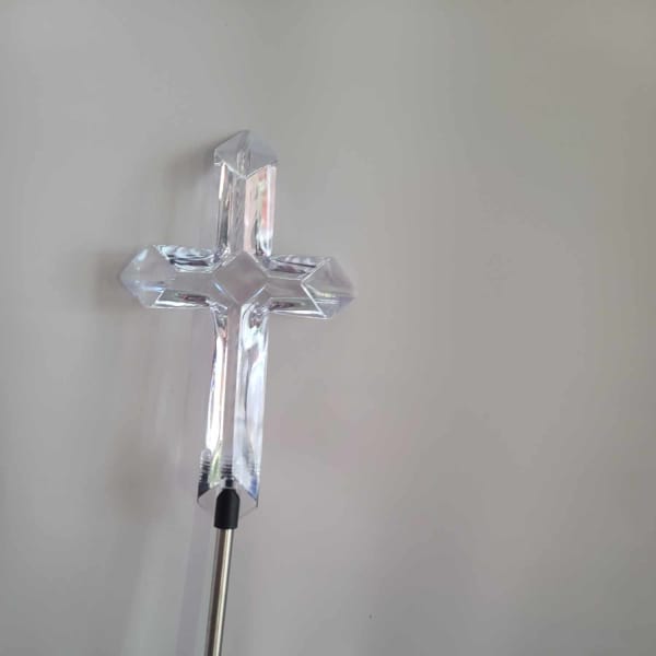 Clear crystal cross on a metal stand against a plain background