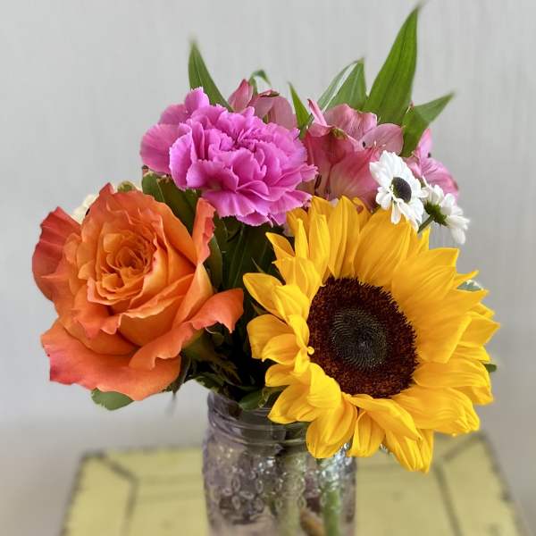 Bouquet of orange roses, pink carnations, and a sunflower in a glass jar