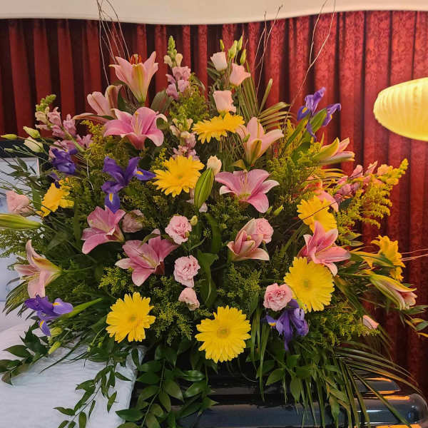 Large floral casket spray with pink lilies, yellow daisies, and purple irises