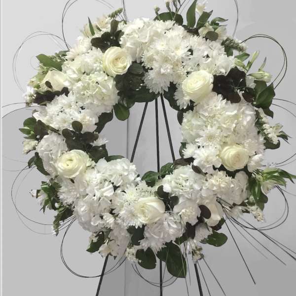 White floral wreath on a black stand with roses and chrysanthemums