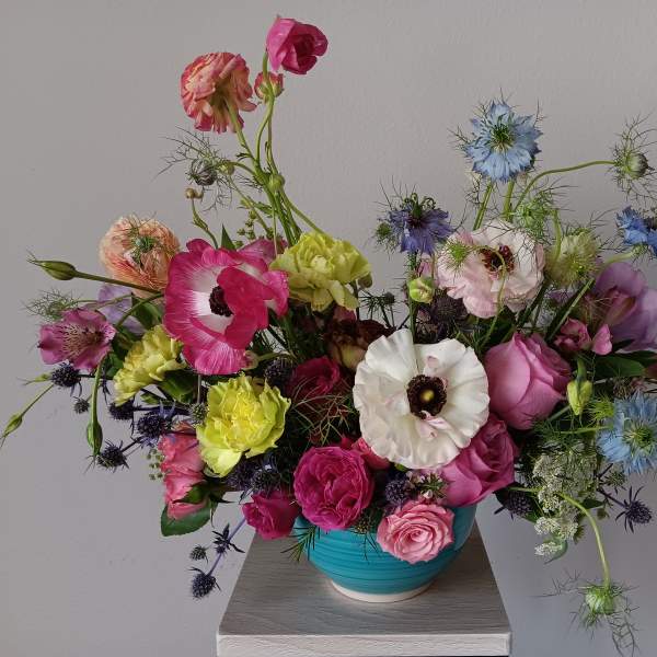 Colorful mixed bouquet in a turquoise vase with pink, white, blue, and yellow blooms