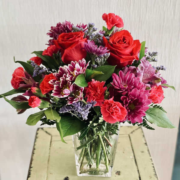 Bouquet of red roses, pink carnations, and purple chrysanthemums in a clear vase