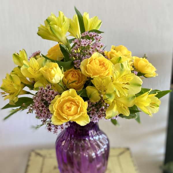 Yellow roses and alstroemeria in a purple glass vase