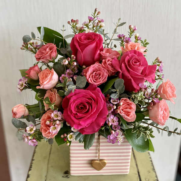 Pink and coral rose bouquet in a striped gift box with a heart charm