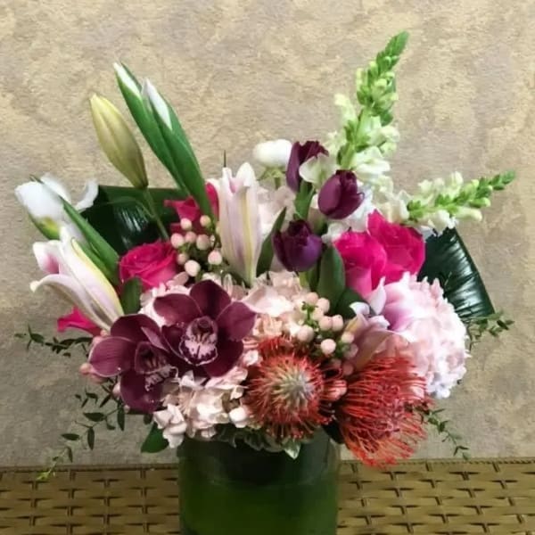 Mixed bouquet with lilies, orchids, roses, and snapdragons in a green vase