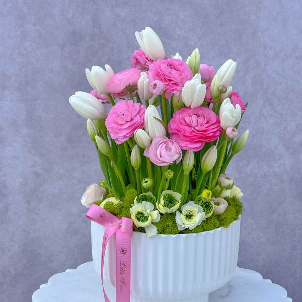 Pink and white flowers arranged in a white vase with a pink ribbon