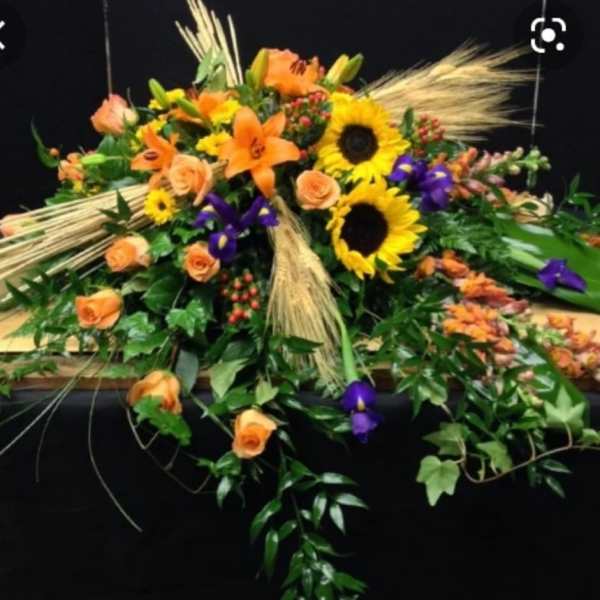 Orange roses and sunflowers arranged with purple flowers and wheat accents