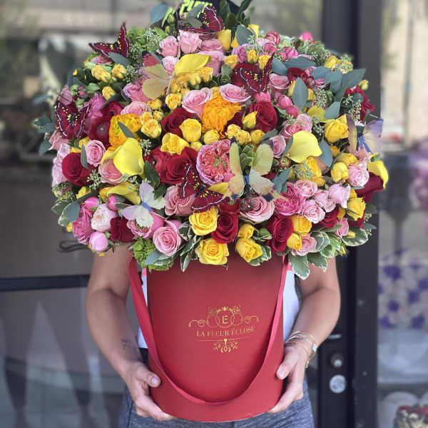 Large bouquet of pink, red, and yellow roses in a red hatbox