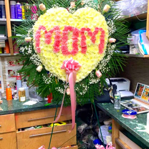 Heart-shaped yellow and pink floral standing arrangement with a pink ribbon