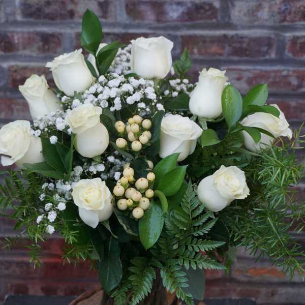 White roses arranged with baby's breath and greenery in a vase