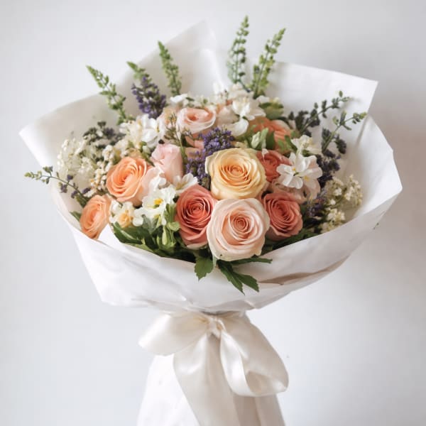 Bouquet of peach and blush roses with white flowers wrapped in white paper