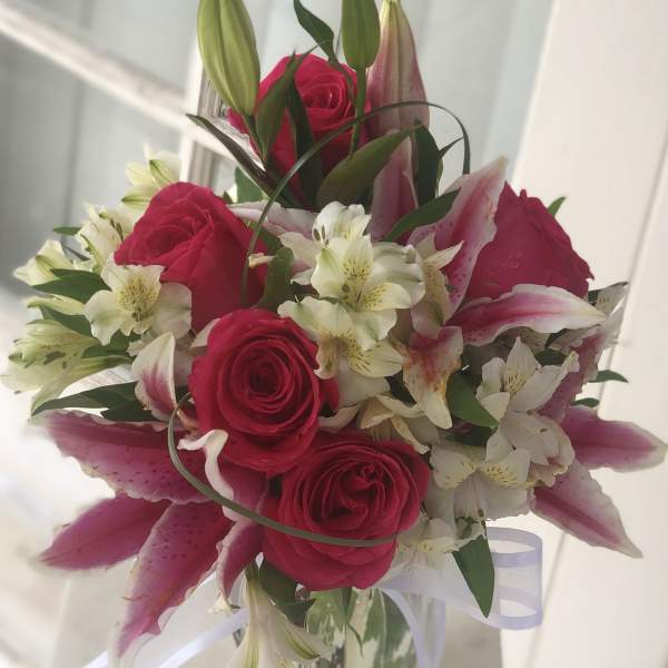 Bouquet of pink roses and lilies in a glass vase with white ribbon
