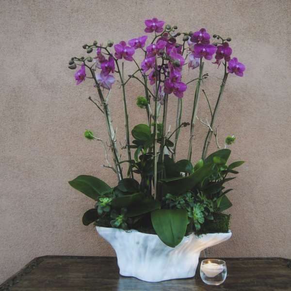 Purple orchids in a white ceramic vase with a small candle beside it