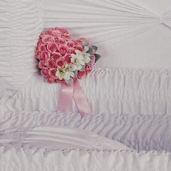 Pink rose bouquet with white flowers and a pink ribbon on a white casket