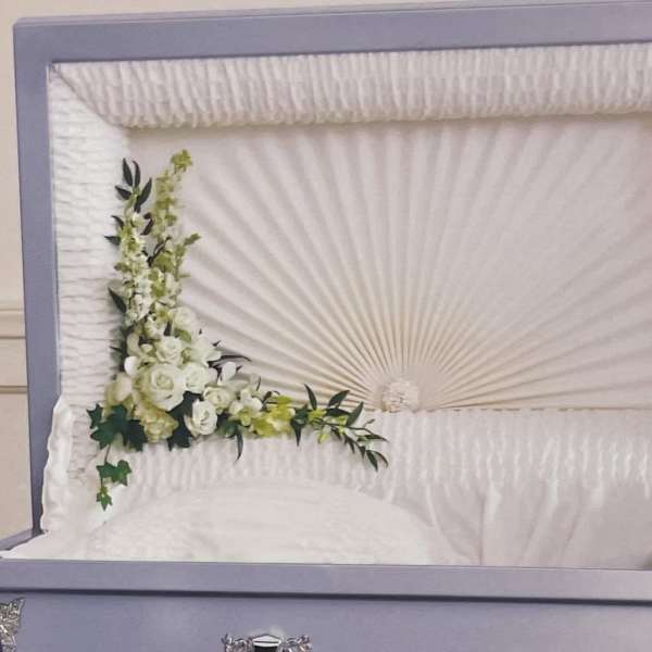 White floral spray on a white casket with green accents