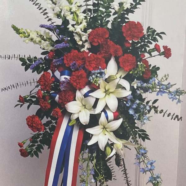 Standing floral spray with red carnations, white lilies, and blue accents
