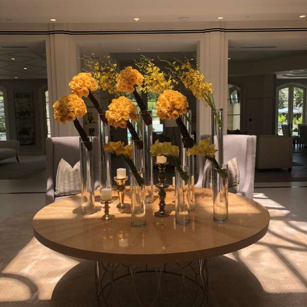 Yellow rose arrangements in tall glass vases on a round table with candles