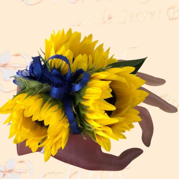 Handheld bouquet of bright yellow sunflowers tied with a blue ribbon