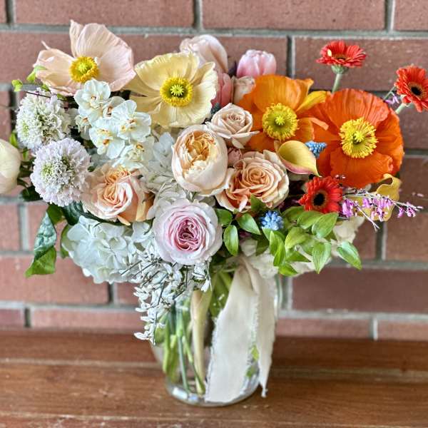 Mixed bouquet of pastel and bright flowers in a clear glass vase