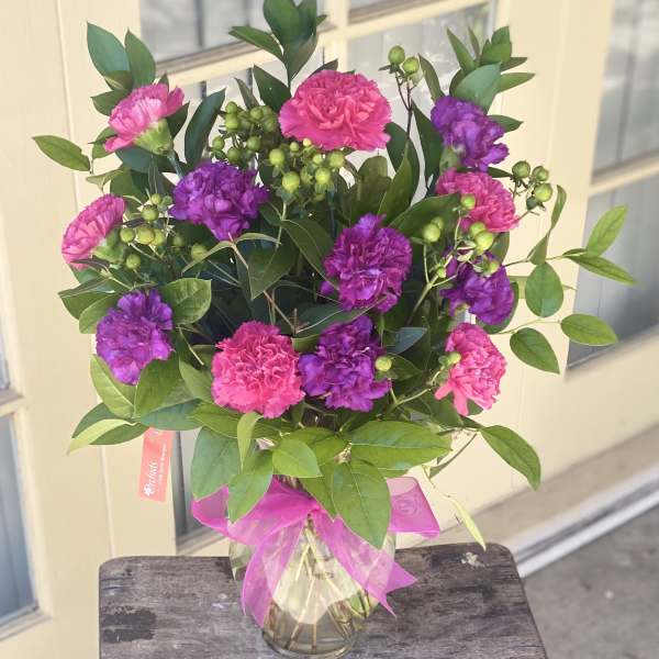 Pink and purple carnations in a glass vase with a pink ribbon