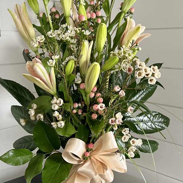 Tall bouquet of pale lilies and white filler flowers in a glass vase with a satin bow