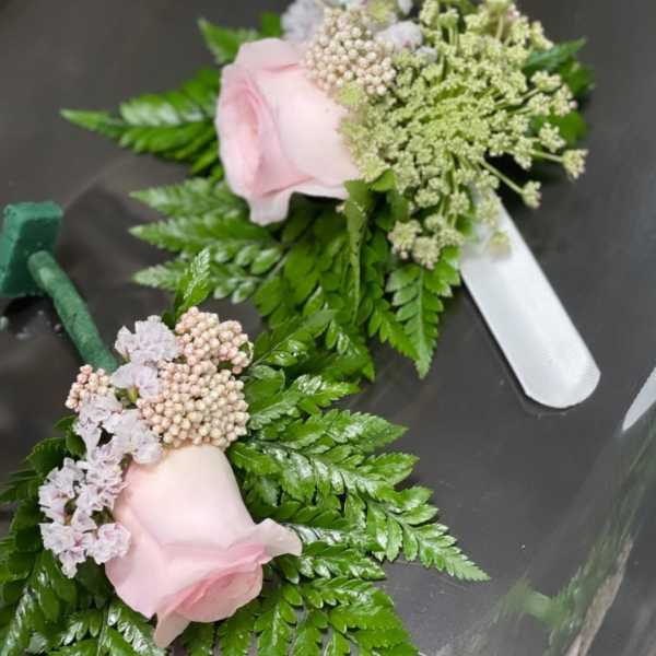 Two pink rose boutonnieres with fern and small filler flowers