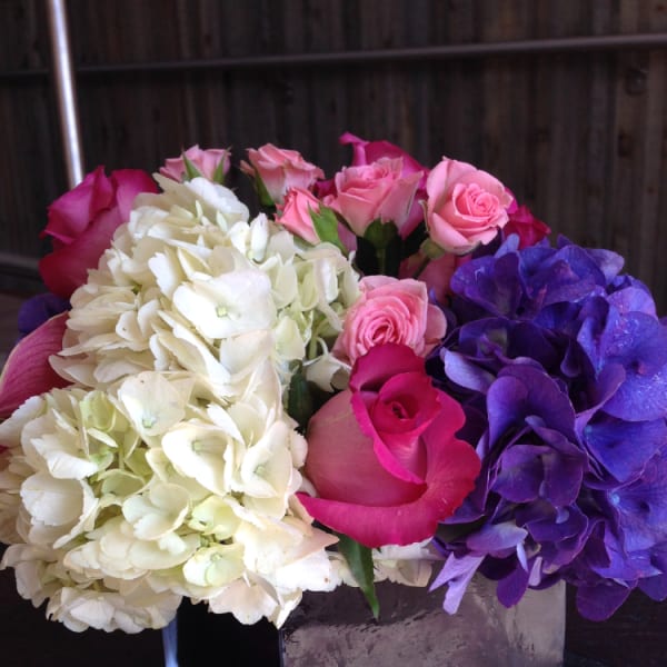 Bouquet of pink roses, white hydrangeas, and purple hydrangeas in a square vase
