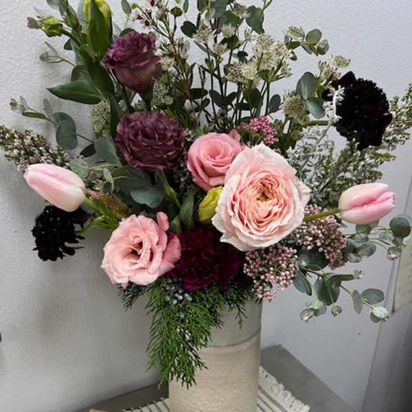 Mixed pink and burgundy bouquet in a tall vase with a box of macarons in front
