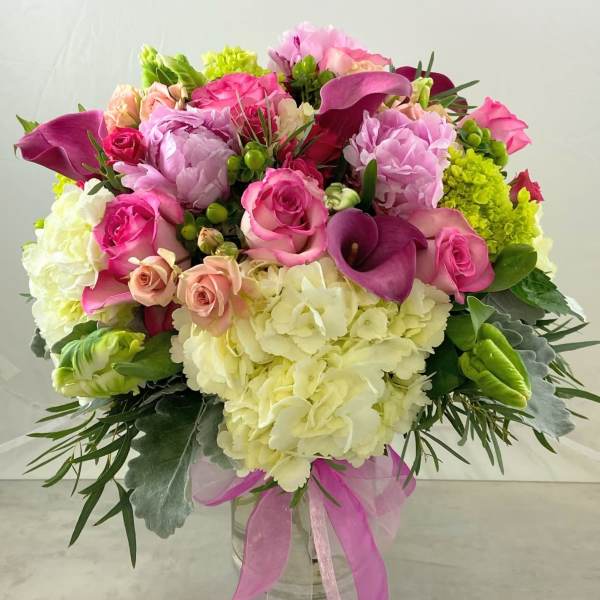 Pink and white mixed bouquet in a clear glass vase with a pink ribbon