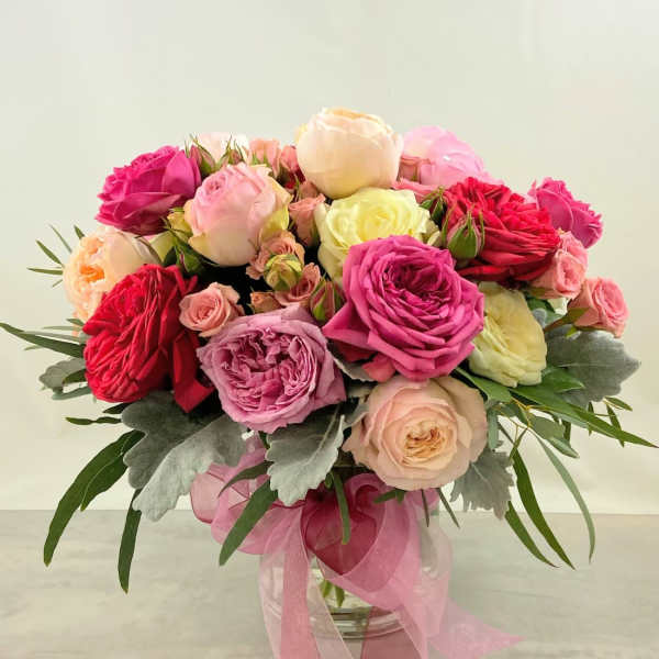 Pink and cream rose bouquet in a glass vase with a pink ribbon