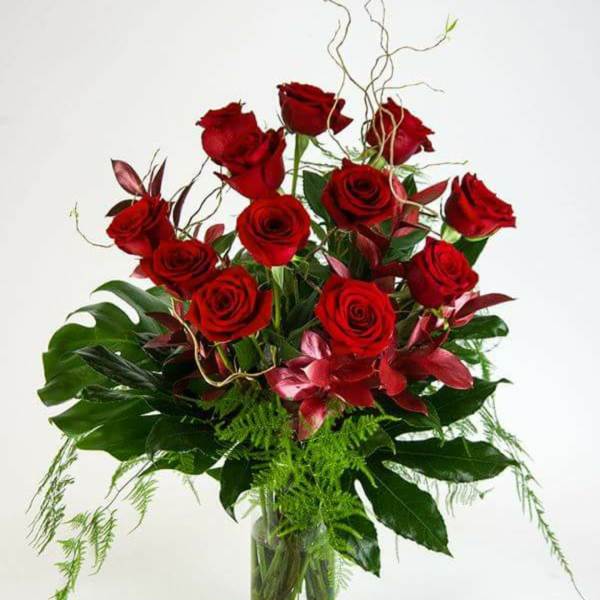 Red roses arranged in a clear glass vase with tropical foliage