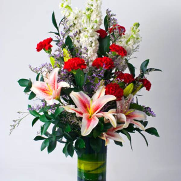 Tall bouquet of lilies and red carnations in a glass vase