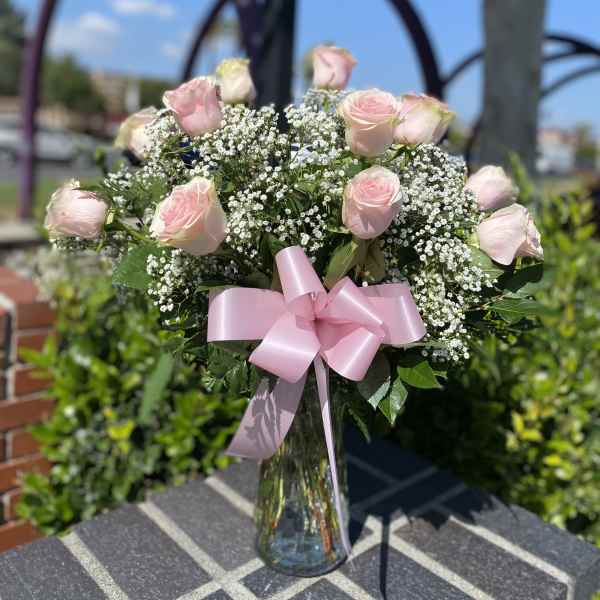 Pink roses and baby's breath in a clear glass vase with a pink ribbon