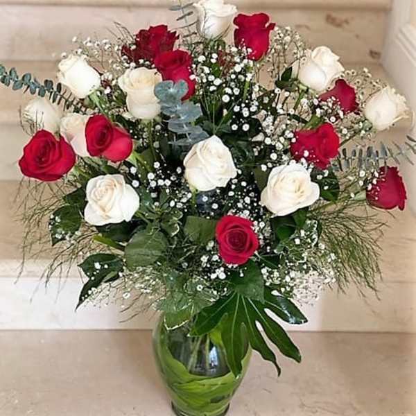 Tall arrangement of red and white roses with baby's breath in a clear glass vase