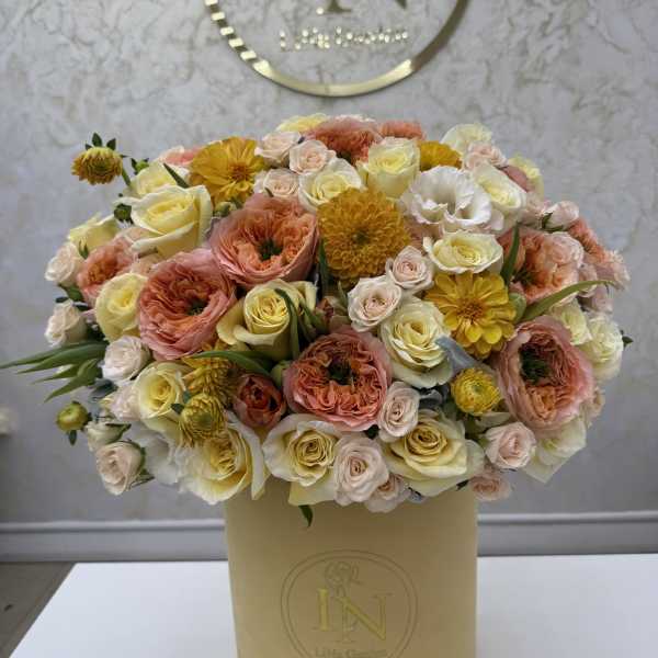 Mixed bouquet of peach, cream, and yellow flowers in a beige hatbox