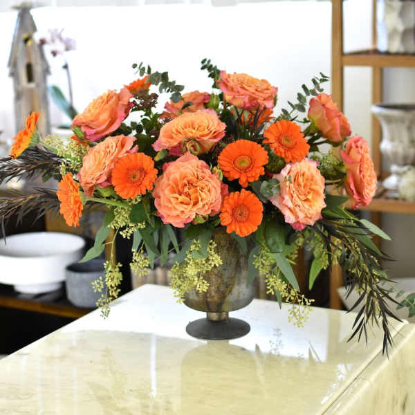 Orange roses and gerbera daisies arranged in a metal vase