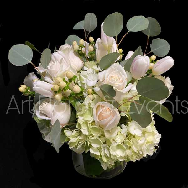 White roses and pale tulips in a glass vase with round eucalyptus leaves