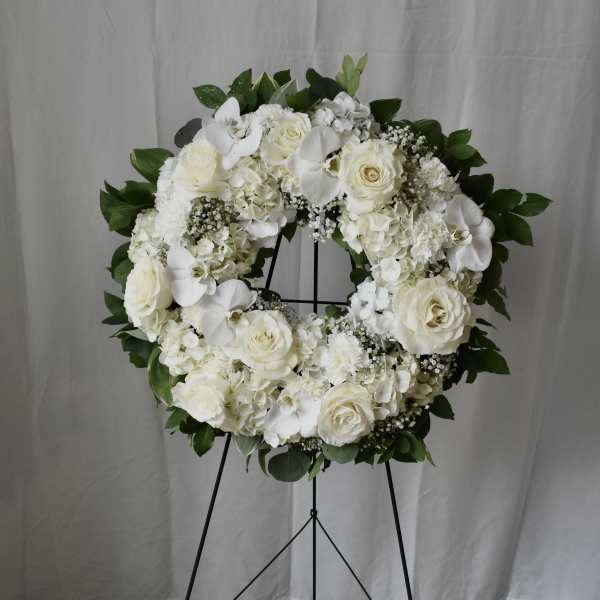 White floral wreath on a black stand with roses and orchids