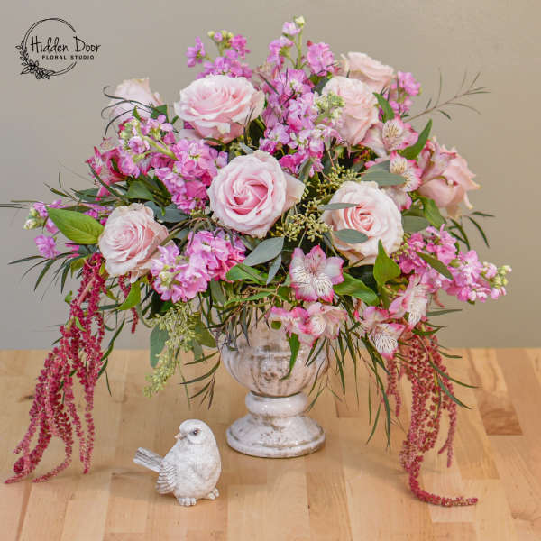 Pink rose arrangement in a white pedestal vase with a small bird figurine
