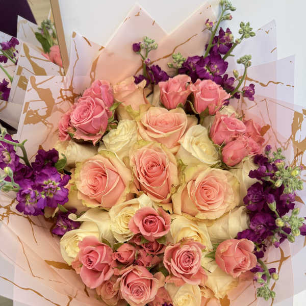 Bouquet of pink and cream roses with purple flowers in decorative wrap