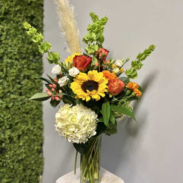 Mixed bouquet in a clear glass vase with sunflowers, roses, hydrangea, and orange blooms