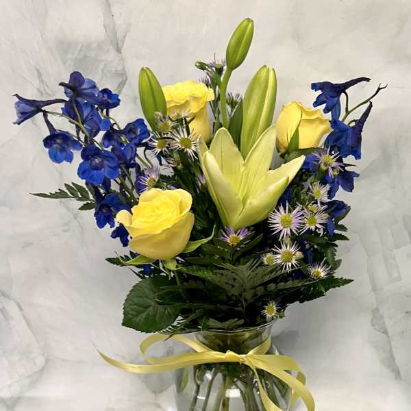 Yellow roses and blue delphinium in a glass vase with a ribbon.