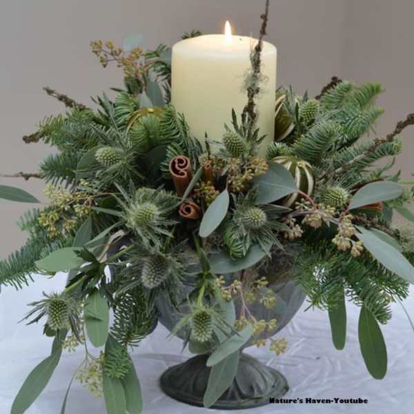 Candle surrounded by a green floral arrangement in a pedestal vase
