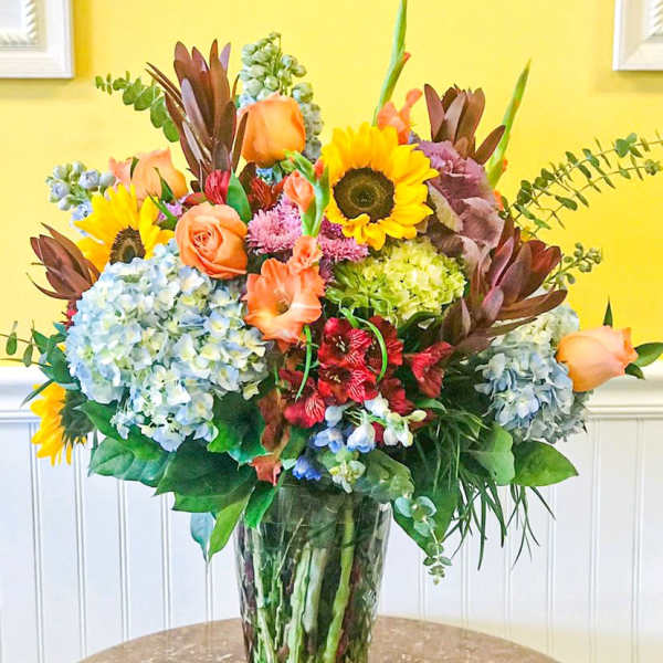 Mixed bouquet with sunflowers, roses, hydrangeas, and lilies in a glass vase