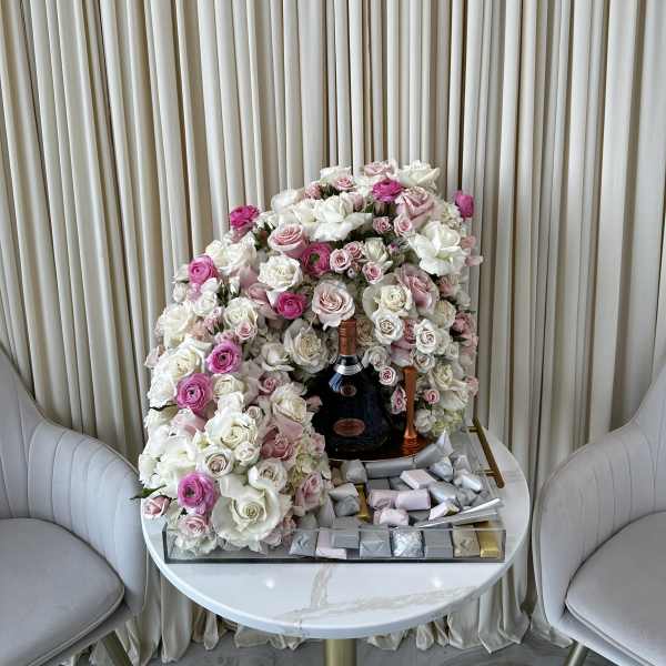 Large pink and white rose arrangement with a champagne bottle and chocolates