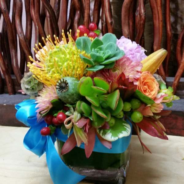 Colorful bouquet with succulents and mixed flowers in a glass vase tied with blue ribbon